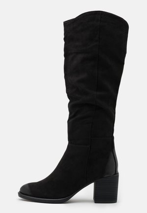 Botte mi-mollet en daim noir avec bout arrondi et talon bloc empilé, accent en cuir lisse au talon sur fond blanc.