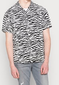 Camicia a maniche corte in tessuto bianco con una fantasia a strisce nere a zebre. Presenta un colletto e una chiusura con bottoni sul davanti.