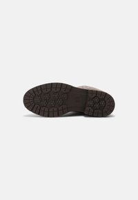 Semelle de chaussure marron foncé avec des crampons profonds et robustes, présentant des motifs hexagonaux et rectangulaires, sur un fond blanc uni.