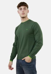 Maglione verde a maniche lunghe con collo rotondo, caratterizzato da accenti verde brillante in contrasto sul colletto e sui polsini. Tessuto morbido.