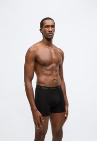 Melni boksa stila apakšbikses ar ērtu pieguļumu, ar zelta krāsas jostu, uz kuras ir uzraksts "HUGO". Izgatavotas no mīksta, elastīga materiāla.