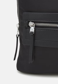 Black nylon backpack featuring a textured leather front pocket, silver zipper hardware, and a branded leather tag.