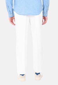 Pantaloni bianchi con una vestibilità dritta, pieghe frontali e una texture liscia. Abbinati a una camicia di jeans azzurri e sneakers.