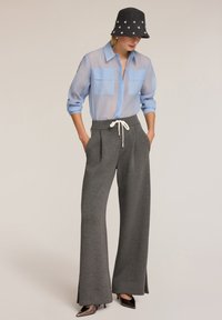Lichtblauwe doorzichtige lang-sleeve shirt met twee borstzakken, in combinatie met grijze wijde sweatpants met een witte koord. Zwarte versierde pet.