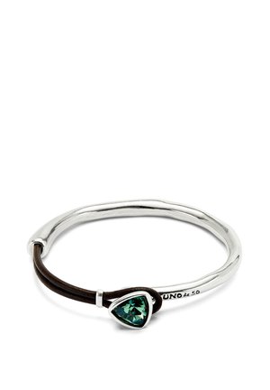 Pulsera de plata con forma irregular, cordón de cuero marrón y acento de gema verde en forma triangular, grabada con el logo de "UNO de 50".