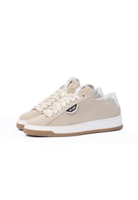 Beige suede sneakers with textured surface, round toe, and white midsole. Features thick laces and a small black logo tag. Brown rubber outsole.