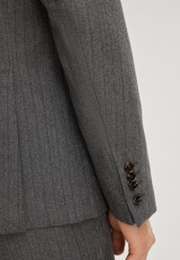 Manica di giacca di suit grigio a righe sottili con tessuto testurizzato, caratterizzata da quattro bottoni scuri al polso e una vestibilità su misura.