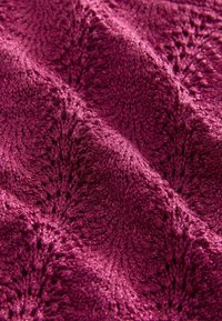 Magentafarbener Textilstoff mit schimmerndem Finish, der ein gestricktes Muster mit feinen Löchern und wellenartigen Designelementen aufweist.