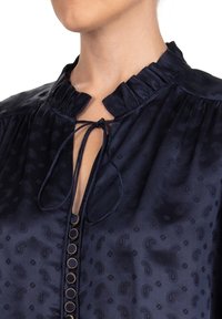 Navy blouse van satijnmateriaal met een gerimpelde kraag, striksluiting en gouden knoopaccenten aan de voorkant, met een paisleypatroon door het hele shirt.