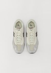Zapatillas New Balance con una combinación de colores crema y gris, materiales de malla y gamuza, puntera redondeada y acentos de logotipo destacados.