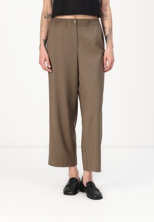 Brown, wide-leg trousers with a relaxed fit, featuring an elastic waistband and front button closure. Worn with black slip-on shoes.