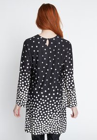 Schwarze Tunika mit weißen Punkten, rückseitigem Schlitz-Detail, langen Ärmeln, weichem Stoff und einem Farbverlauf-Muster von großen zu kleinen Punkten.