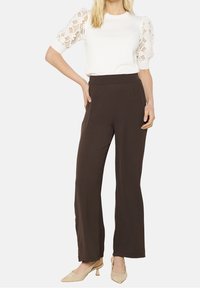 Vit topp med spetsiga puffärmar, matchad med bruna vida byxor. Tyget ser mjukt ut; byxorna har sidofållar och hög midja.