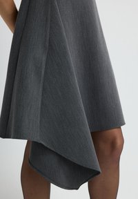 Graues asymmetrisches Kleid aus glattem, strukturiertem Stoff, mit einem drapierten Saum und sauberem Finish. Akzentuiert durch eine schlanke Silhouette.