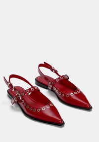 Rote Leder Slingback Ballerinas mit spitzen Zehen, silbernen Ösenakzenten, doppelten Riemen und einer flachen schwarzen Sohle. Glatte Textur und minimalistisches Design.