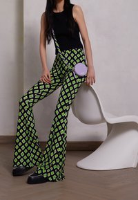 Spodnie dzwony z czarnego materiału w zielono-białe wzory w diamenty; zestawione z czarnym topem na ramiączkach i okrągłą fioletową torebką na łańcuszku.