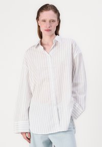 White button-up shirt with blue stripes, long sleeves, oversized fit, and a classic collar. Soft cotton material with a slightly sheer texture.
