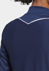 Marineblaues Poloshirt mit strukturiertem Muster, einem kontrastierenden weißen Akzent am Kragen und kurzen Ärmeln.