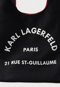 Fekete szövet táska fehér felirattal, amelyen az "KARL LAGERFELD PARIS" és a "21 RUE ST-GUILLAUME" íves formában van nyomtatva.