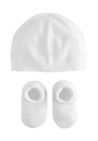 Bonnet en tricot blanc avec un sommet arrondi et un ourlet côtelé, associé à des chaussons assortis en velours doux dotés d'ouvertures élastiques pour un ajustement sécurisé.
