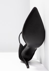 Černá semišová vysoká bota na podpatku s špičatou špičkou a štíhlým stiletto podpatkem, s texturovanou černou podrážkou a otevřeným designem vzadu.