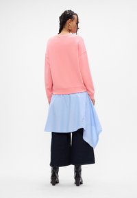 Rosa genser med senkede skuldre, lagd over en blåstripet skjorte, kombinert med vide mørke denimjeans og svarte hælsko.