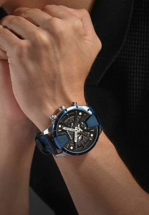 Orologio cronografo nero e argento con accenti blu, cinturino in gomma testurizzata, più quadranti e hardware metallico sul lato.