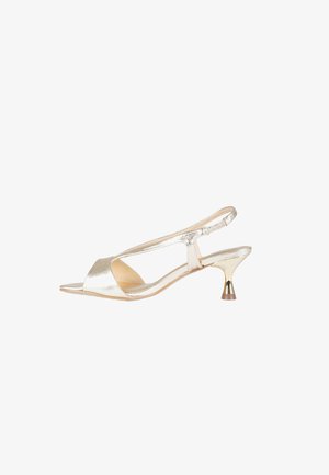 Scarpa slingback aperta lucida dorata con tacco basso kitten e design traforato su sfondo bianco.