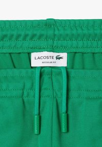 Grønne Lacoste shorts med snoreliv, regulær pasform og mærkater syet ind i stoffet, der fremhæver den glatte tekstur.