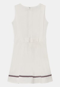 Ärmös vit klänning med en figursydd liv och utsvängd kjol. Anmärkningsvärda detaljer inkluderar en dragkedja i ryggen och horisontella randiga detaljer vid fållen.