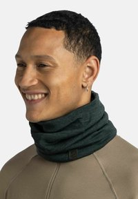 Dark green neck gaiter made of soft fabric, featuring a smooth texture and a logo tag. Worn snugly around the neck.