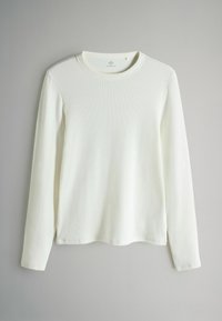 Długi rękaw, okrągły dekolt w białym, ribbowanym materiałem. Posiada prosty krój z bocznymi rozcięciami u dołu oraz miękką, teksturowaną powierzchnię.