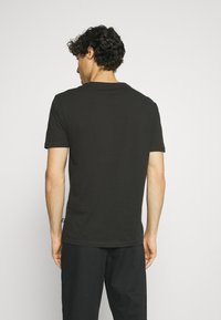 Black short-sleeve t-shirt in cotton, round neckline, features clean design with no patterns, shown from the back with simple stitching details.