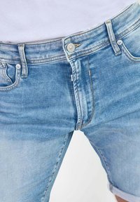 Shorts de mezclilla azul claro con un diseño clásico de cinco bolsillos, que presentan un leve desgaste, una cremallera y dobladillos enrollados en las extremidades.