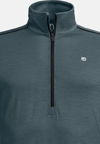 Teal pullover top featuring a high collar, half-zip front, and black accent stitching. Fabric has a smooth, textured finish. Logo detail included.