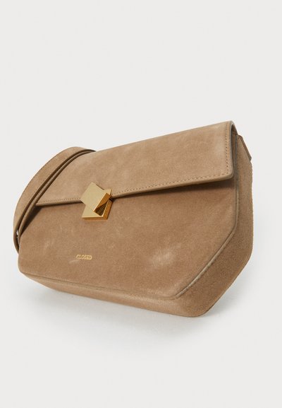 Tan suede crossbody taske med klap, gylden geometrisk spænde og prægede logo. Har en subtilt tekstureret overflade og vinklet design.