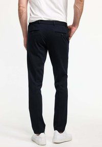 Námořnické modré slim-fit kalhoty s dvěma zadními kapsami, páskovými smyčkami a hladkou texturou; kombinované s bílými teniskami na neutrálním pozadí.