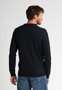 Pulover lung cu maneci lungi, de culoare neagră, cu guler rotund și un model texturat, asortat cu blugi din denim albastru.