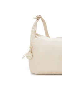 Beige shoulder bag with knotted handle, a circular logo patch, and a monkey-face zipper pull charm.