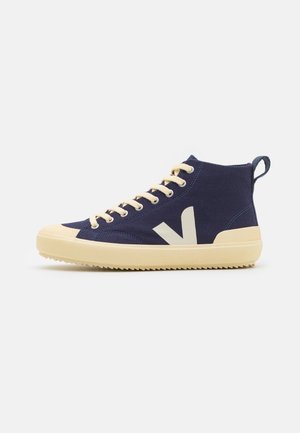 Baskets montantes bleu marine avec lacets, semelle et embout couleur crème, avec un logo "V" crème sur le côté et une languette à l'arrière.