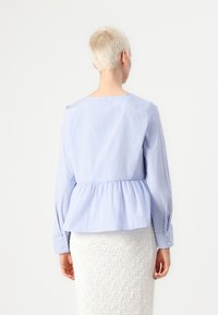Modra in bela prugasta peplum bluzka z dolgimi rokavi in gumbnimi manšeti, ki ima okroglo ovratnico in nabirjeno podrobnost v pasu.