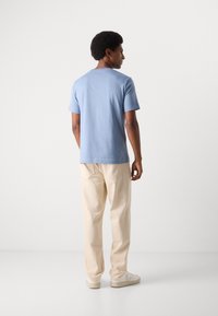 Tricou din bumbac, de culoare albastru deschis, cu mâneci scurte, asortat cu pantaloni crema și adidași crema. Croială simplă, lejeră.
