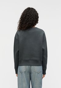 Σκούρο γκρι φούτερ με στρογγυλή λαιμόκοψη και ελαστική ρίγα στο κάτω μέρος. Μαλακή υφή και άνετη εφαρμογή, σε συνδυασμό με ανοιχτό μπλε τζιν παντελόνι.