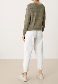 Pull en maille vert olive avec rayures texturées, assorti à un pantalon blanc taille haute et des baskets beige clair ; détails visibles à l'arrière.