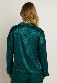 Ensemble de vêtements d'intérieur en satin teal avec un motif zèbre subtil ; comprend un haut à col, à manches longues et un pantalon assorti, texture lisse, coupe décontractée.
