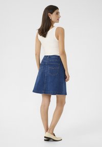 Denim A-linje kjol i mörkblått med bakfickor och detaljer i kontrastsöm; kombinerad med en vit ärmlös topp och krämfärgade loafers.