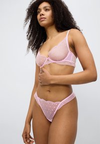 Σετ ροζ εσώρουχα με διάφανο δαντελένιο σουτιέν με σχέδια καρδιές και ταιριαστό στρινγκ. Διακοσμη μένο με λεπτά βολάν κατά μήκος των άκρων.
