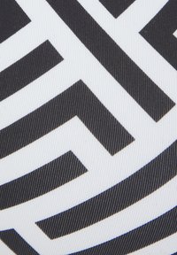 Tissu noir et blanc présentant un motif géométrique audacieux avec des designs angulaires. La texture semble lisse avec un léger grain.