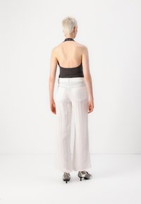 Čierna halterneck top, biele textúrované široké nohavice s vreckami a strieborné nízkopodrážkové topánky. Model zobrazený zozadu na bielom pozadí.