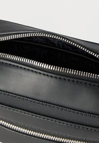 Κοντινή εικόνα μερικώς ανοιχτού ασημένιου φερμουάρ σε μαύρη δερμάτινη και υφασμάτινη τσάντα ή θήκη, που δείχνει την ομαλή υφή και τις λεπτομέρειες ραφής.